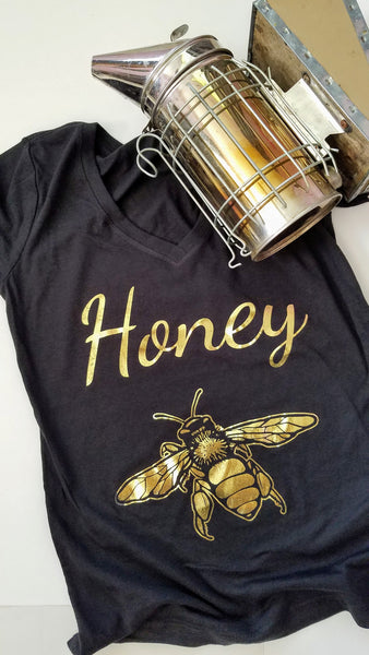 Gold Honey Bee Women's T-shirt. Make a statement and look your best in this fabulous gold foil tee. Soft cotton makes this shirt easy to wear. The bright crisp gold design is the perfect addition to your sunny spring wardrobe.   Limited edition. Wash gentle inside out and hang dry.  Cotton/poly blend, laundered, tearaway label, form fitted. Can size up.